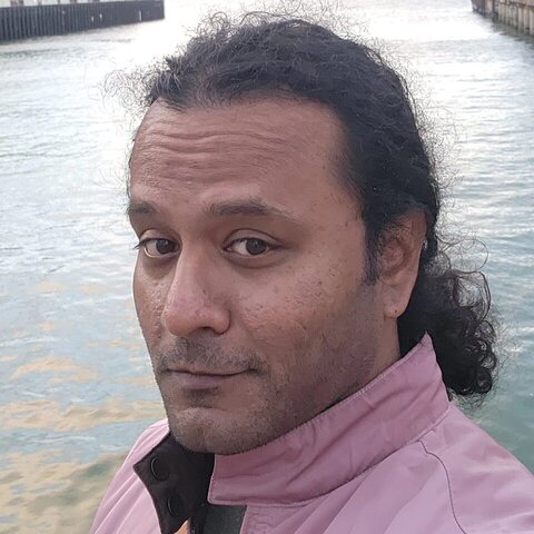 Srix at a pier in San Francisco, pink jacket, looking at the camera